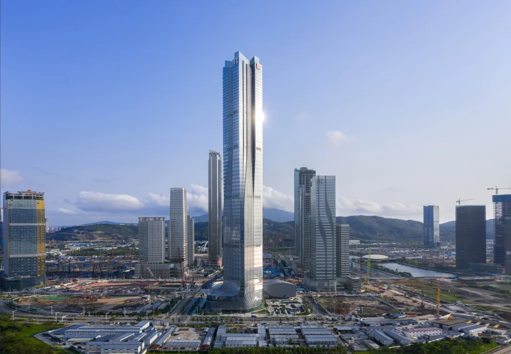 Aedas’ Hengqin International Financial Center in Zhuhai is shown as a sculptural super‑tall tower with four vertical volumes converging into a single crystalline form. The image highlights a sleek glass façade with subtle setbacks and a refined podium, embodying the “Nine Dragons” concept to express convergence, growth, and momentum, while anchoring a new financial skyline within the Greater Bay Area.