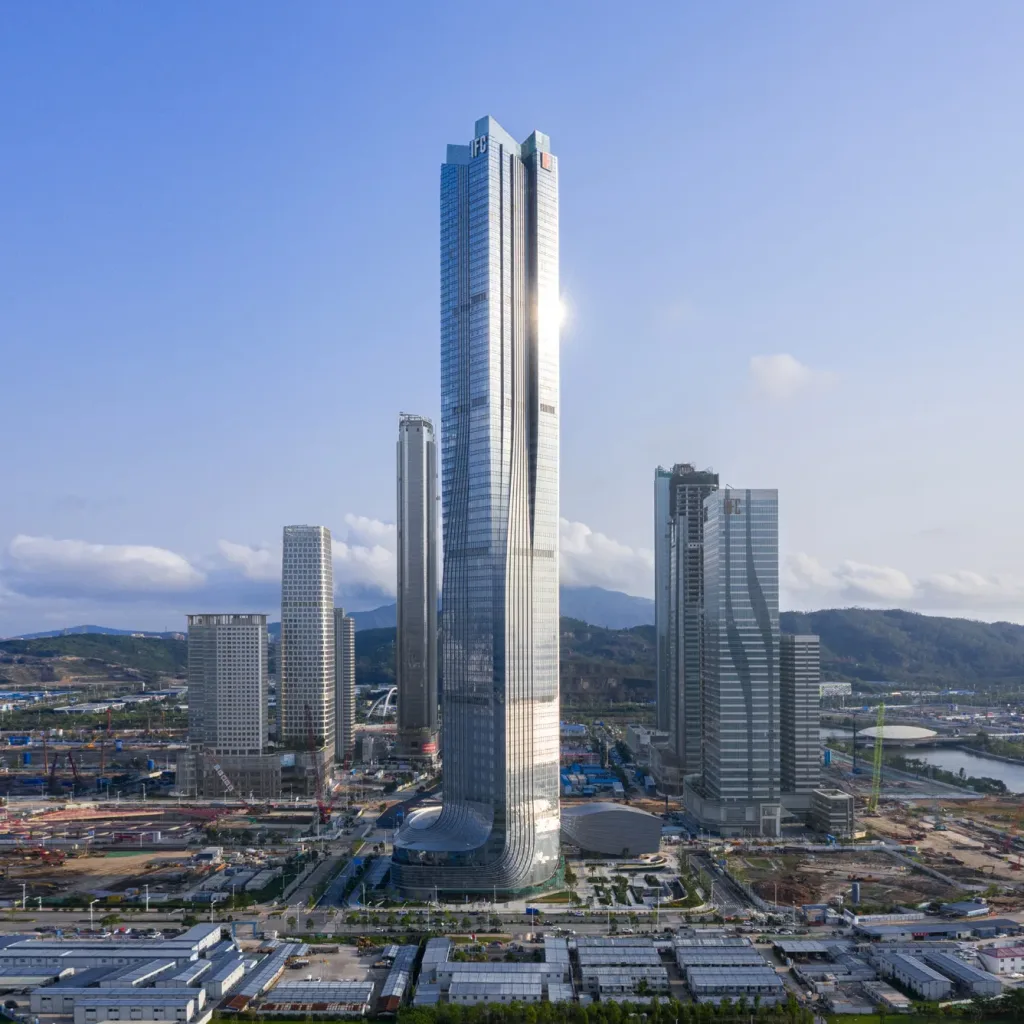 Aedas’ Hengqin International Financial Center in Zhuhai is shown as a sculptural super‑tall tower with four vertical volumes converging into a single crystalline form. The image highlights a sleek glass façade with subtle setbacks and a refined podium, embodying the “Nine Dragons” concept to express convergence, growth, and momentum, while anchoring a new financial skyline within the Greater Bay Area.
