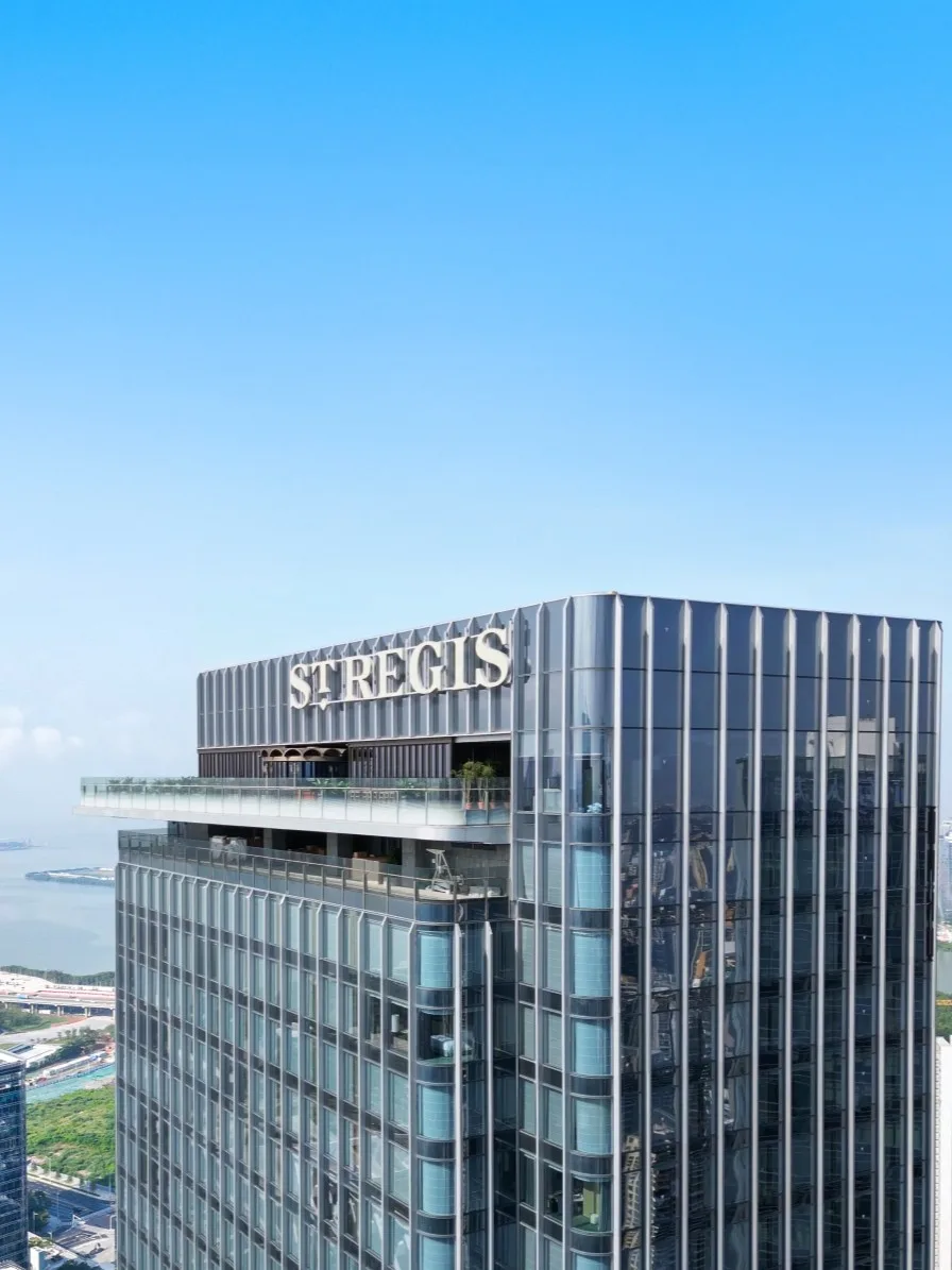 Aedas’ OCT Real One / Ruiwan Tower with vertical ribbed aluminium façade and glazed curtain wall overlooking Qianhai Bay in Shenzhen. High-rise tower by Aedas featuring a slender rectilinear form clad with glazed curtain wall systems and continuous vertical aluminium ribbing. The tower rises from a mixed-use podium with recessed glazing, set within a coastal urban district overlooking Qianhai Bay. Surrounding infrastructure and greenery indicate integration with a waterfront and central green axis.