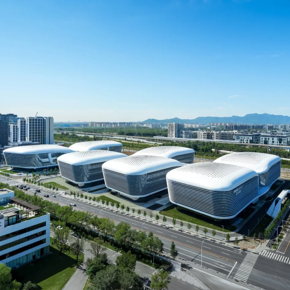 Aedas’ SINOVAC high‑tech campus with clustered R&D and manufacturing buildings linked by elevated corridors. Aerial view of an Aedas‑designed science and technology campus comprising multiple low‑rise, rounded‑corner building volumes with continuous horizontal glazing bands. The buildings are arranged in parallel rows and linked by elevated corridors above landscaped grounds. Wide internal roads, green buffers and adjacent metro and expressway infrastructure frame the campus within a suburban innovation district.
