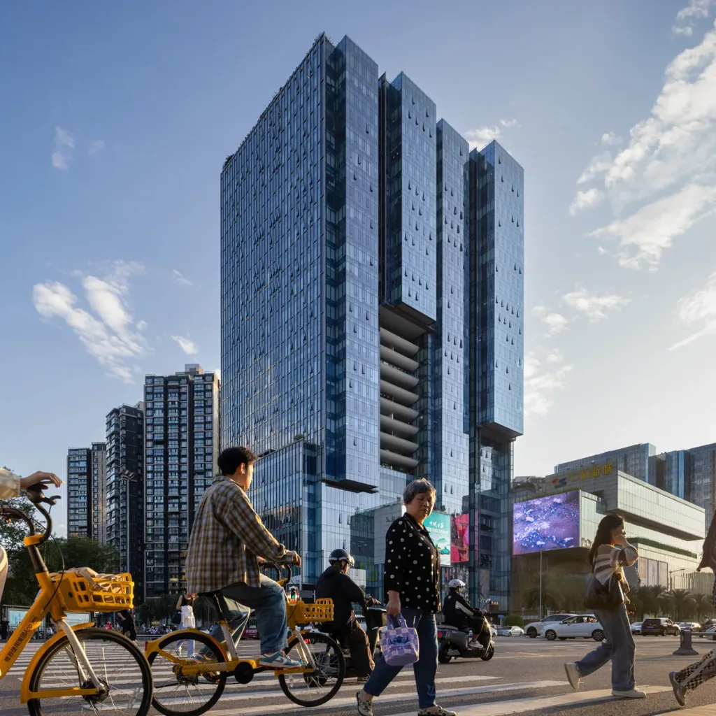 Aedas’ Chengdu mixed‑use development with layered office tower, serviced apartments and a terraced retail podium. Aerial view of an Aedas‑designed mixed‑use complex in Chengdu, showing a tall office tower with staggered, slice‑shaped floor plates rising from a multi‑storey retail podium. Serviced apartment towers are positioned along the site edge. Extensive glass curtain walls, stepped massing, and rooftop terraces frame major urban roads and surrounding residential districts.
