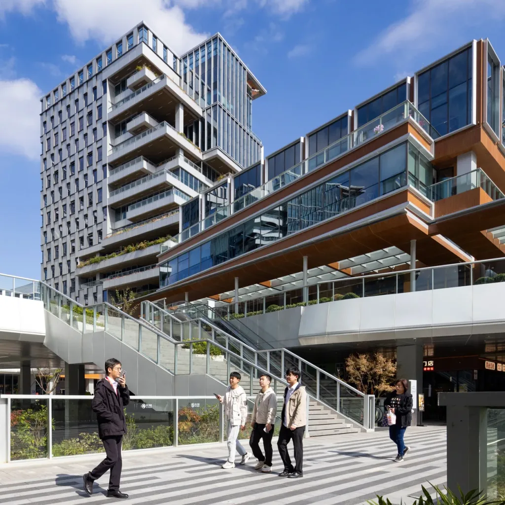 Aedas’s Golden Union Park in Shanghai is shown as a contemporary office campus with stepped low‑rise buildings, terraced outdoor workspaces, and mid‑rise towers rising from a landscaped public plaza. The ground‑level view highlights transparent façades, multi‑level pedestrian circulation, and the integration of office architecture with park‑like open space.