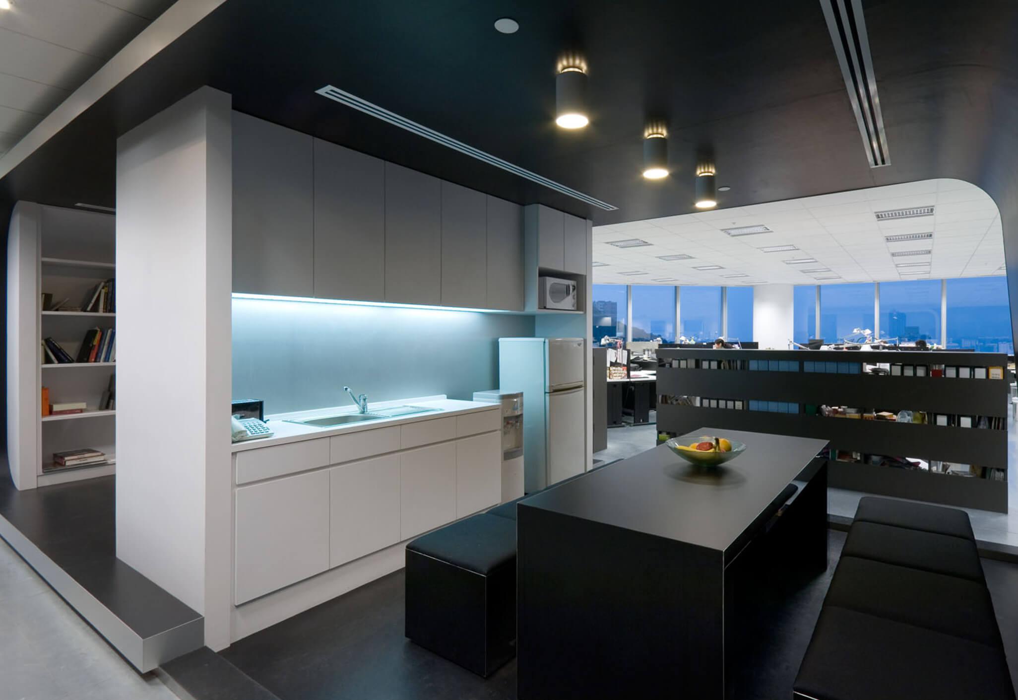 Aedas Interiors’ M&C Saatchi Hong Kong office is shown as a bold monochromatic workplace with black and white finishes, exposed raised‑floor panels, and minimalist kitchen and breakout areas. The image highlights cost‑efficient interior architecture using restrained materials, integrated lighting, and open planning to create a strong brand identity without physical separation between reception and open office zones.