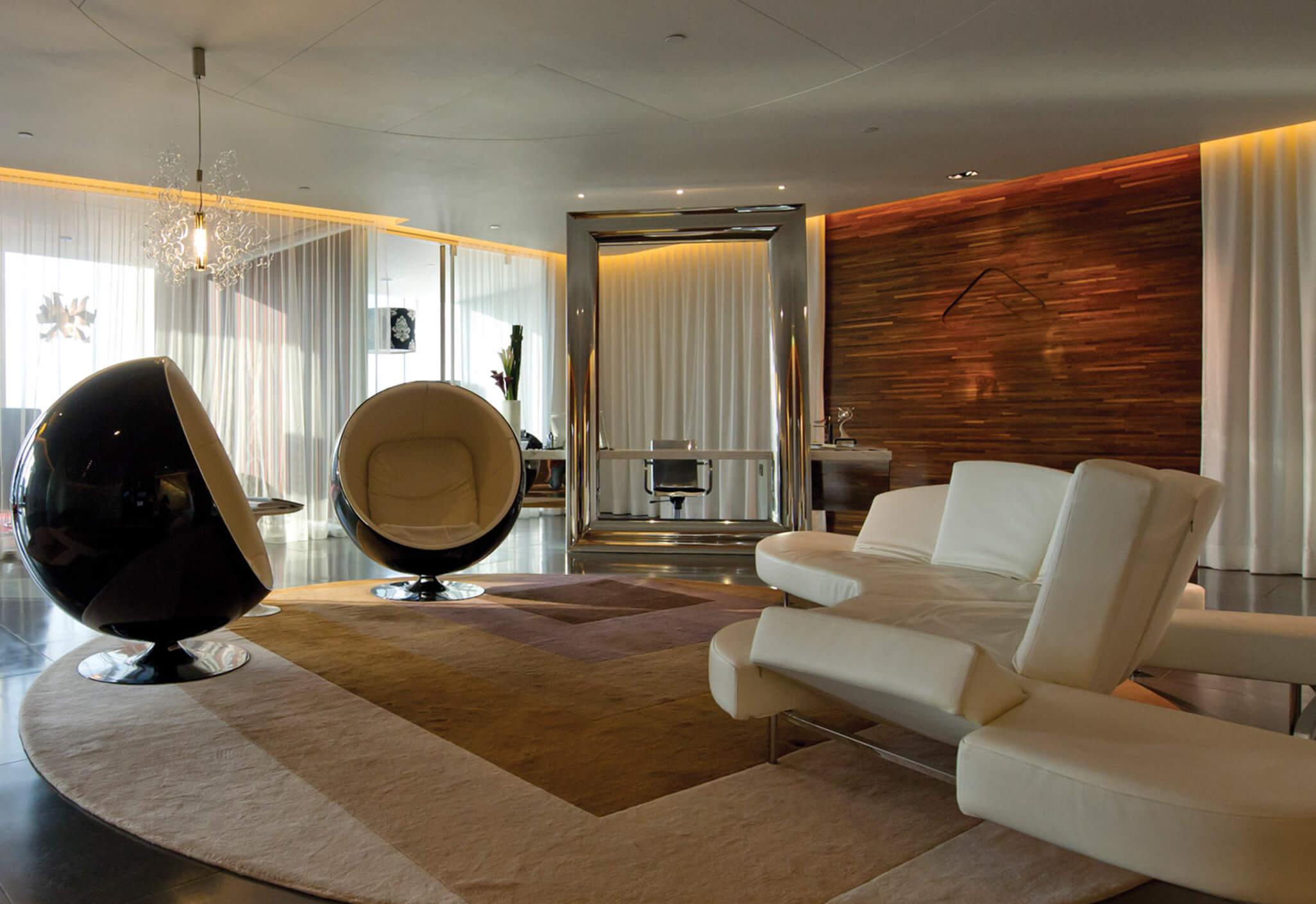 Aedas Interiors’ Hong Kong Office at One Island East is shown as a refined, hospitality‑inspired workplace lounge featuring sculptural seating, layered soft furnishings, a feature timber wall, and ambient concealed lighting. The image highlights a sophisticated interior environment that blends residential comfort with professional workspace, encouraging cross‑disciplinary interaction and creative exchange within a large design studio setting.