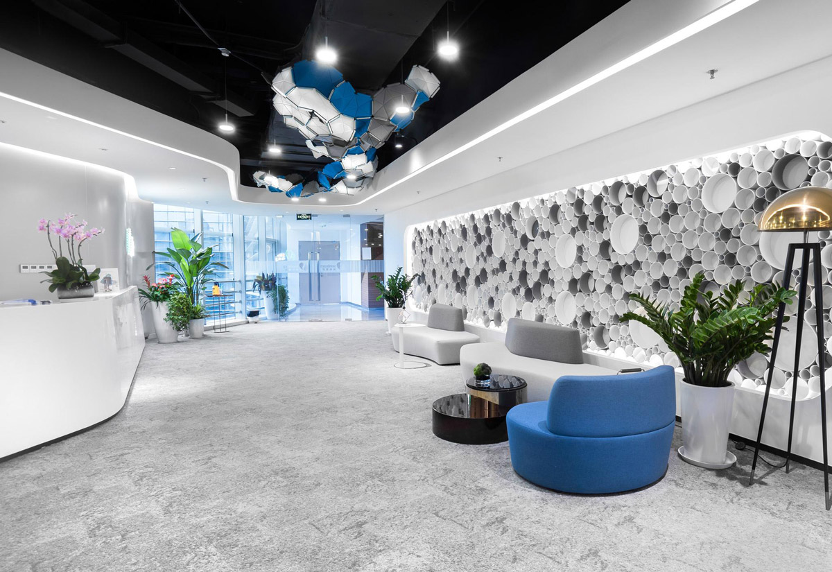 Aedas Interiors’ Sembcorp International Waterhub in Nanjing is shown as an experiential interior featuring a sculptural ceiling installation, textured feature wall of circular elements, integrated greenery, and lounge seating. The image highlights sustainability‑driven interior design combining high‑tech exhibition space with nature‑inspired materials and forms.