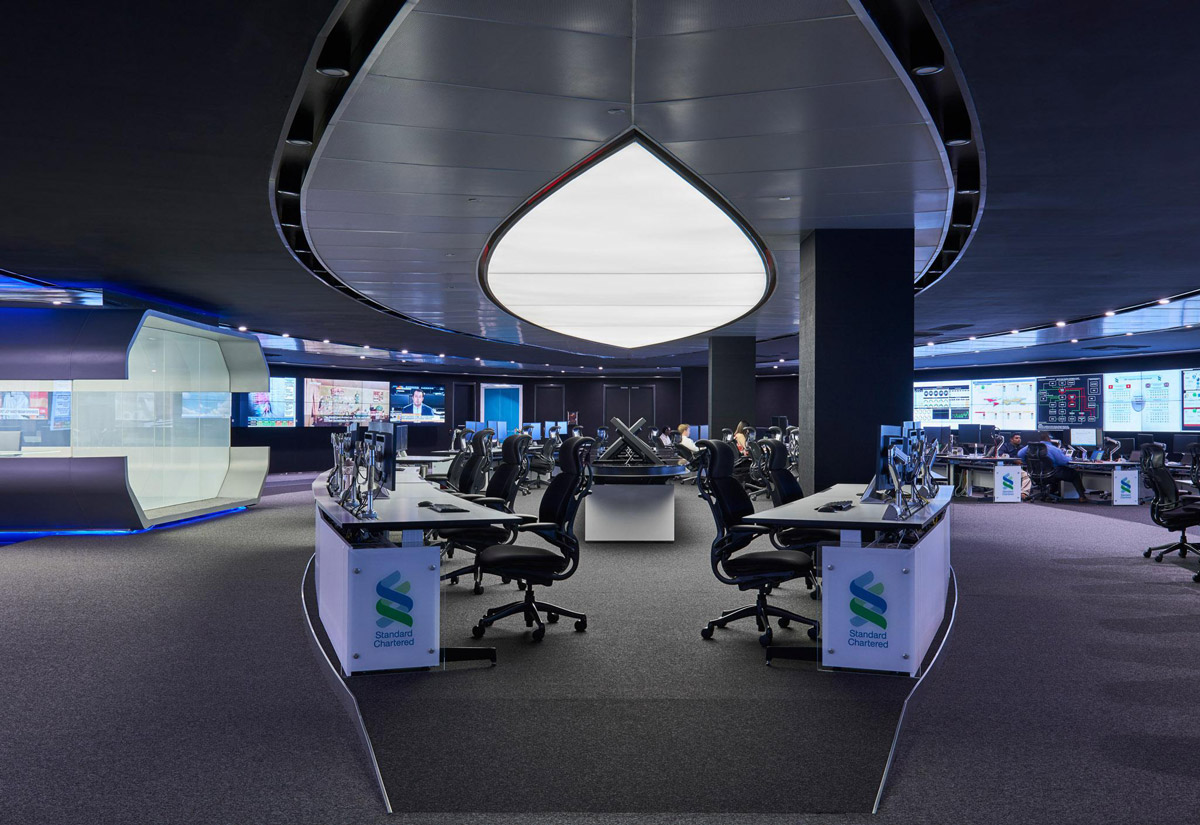 Aedas Interiors’ Standard Chartered Bank Global Command Centre in Kuala Lumpur is shown as a highly secure, fully digitised operations space with radial workstation clusters, immersive multi‑screen monitoring walls, and a sculptural fingerprint‑inspired ceiling form. The image highlights futuristic interior architecture designed for global network control, real‑time data visualisation, and visitor engagement within a mission‑critical banking environment.