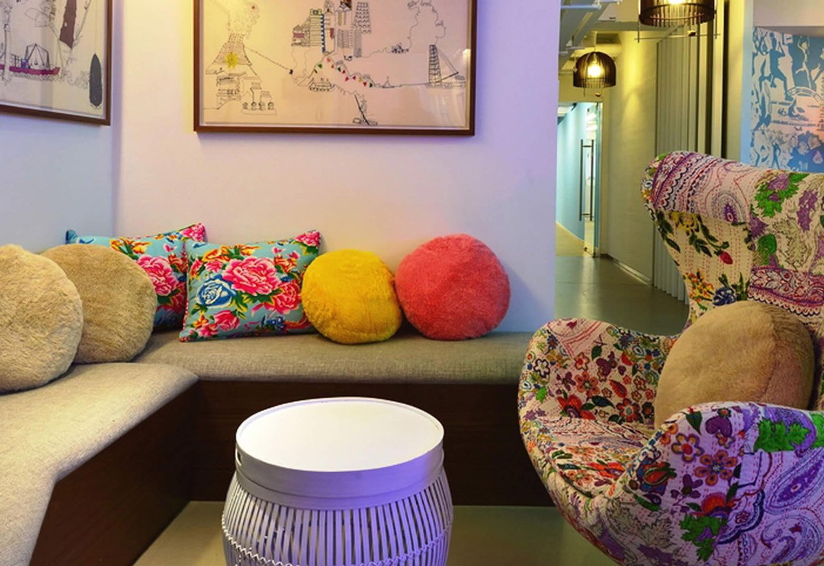Aedas Interiors’ Pentland Asia Headquarters in Hong Kong is shown as a relaxed collaborative lounge featuring upholstered seating, colourful textile cushions, and a patterned feature armchair. The image highlights a warm, brand‑driven interior inspired by fabric texture and weave, integrating informal meeting space, curated artwork, and local design elements to create an energetic, human‑centred workplace environment.