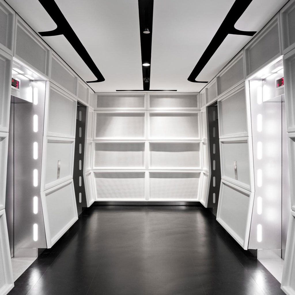 Aedas Interiors’ Lucasfilm Singapore office is shown with a cinematic, Star Wars–inspired lift lobby featuring illuminated vertical light strips, dark polished flooring, and modular wall panels. The image highlights a themed interior environment designed for immersive storytelling, wayfinding through light guidance, and a controlled low‑light workspace supporting frequent collaborative reviews and production workflows.