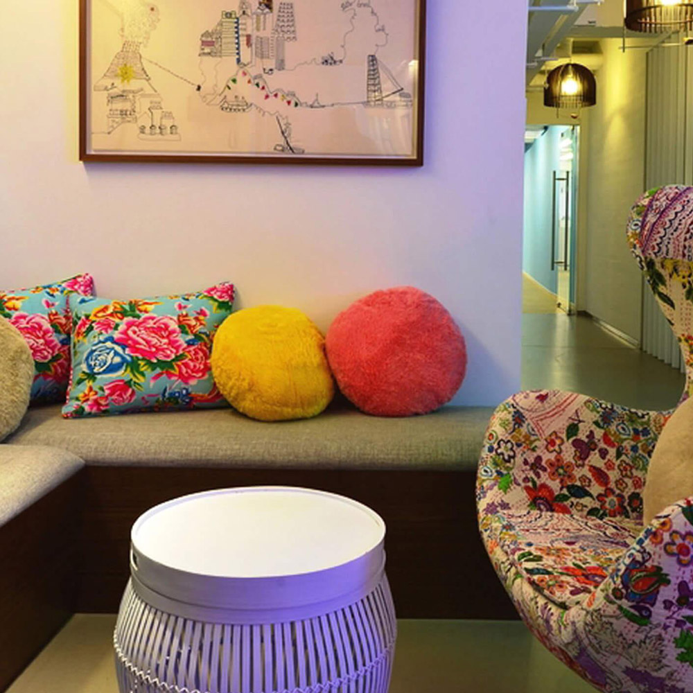 Aedas Interiors’ Pentland Asia Headquarters in Hong Kong is shown as a relaxed collaborative lounge featuring upholstered seating, colourful textile cushions, and a patterned feature armchair. The image highlights a warm, brand‑driven interior inspired by fabric texture and weave, integrating informal meeting space, curated artwork, and local design elements to create an energetic, human‑centred workplace environment.