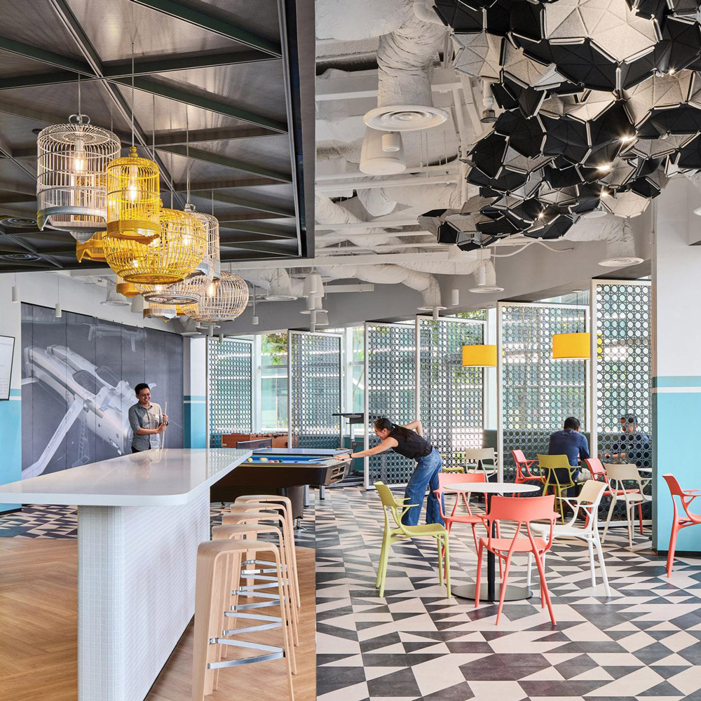 Aedas Interiors’ Autodesk Client Experience Centre in Singapore is shown as a multifunctional collaboration space with geometric ceiling installations, open social seating, a feature bar counter, and patterned flooring. The image highlights adaptive workplace interiors designed to support client engagement, informal collaboration, and creative showcase environments.