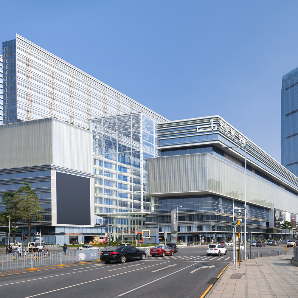 Aedas’ Baoneng Centre in Shenzhen with layered glass façades, multi‑storey podium and high‑rise towers in Sungang. Street‑level view of Aedas‑designed Baoneng Centre in Shenzhen, showing an expansive mixed‑use complex with a multi‑storey podium articulated by layered glass curtain walls and horizontal bands. Above, a tall Grade‑A office tower and ancillary towers rise from the podium, while glazed atrium volumes and urban streetscape interfaces define the development’s public edge.
