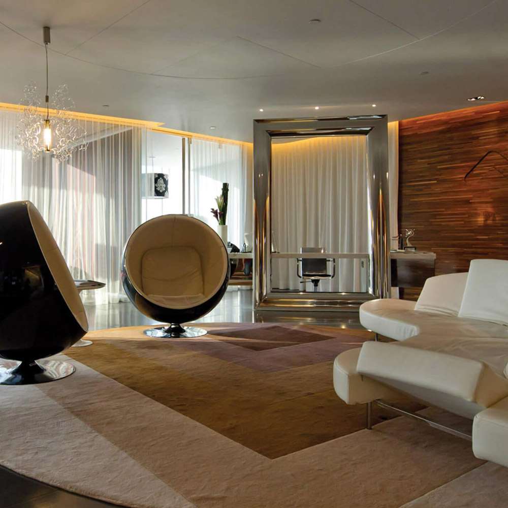 Aedas Interiors’ Hong Kong Office at One Island East is shown as a refined, hospitality‑inspired workplace lounge featuring sculptural seating, layered soft furnishings, a feature timber wall, and ambient concealed lighting. The image highlights a sophisticated interior environment that blends residential comfort with professional workspace, encouraging cross‑disciplinary interaction and creative exchange within a large design studio setting.