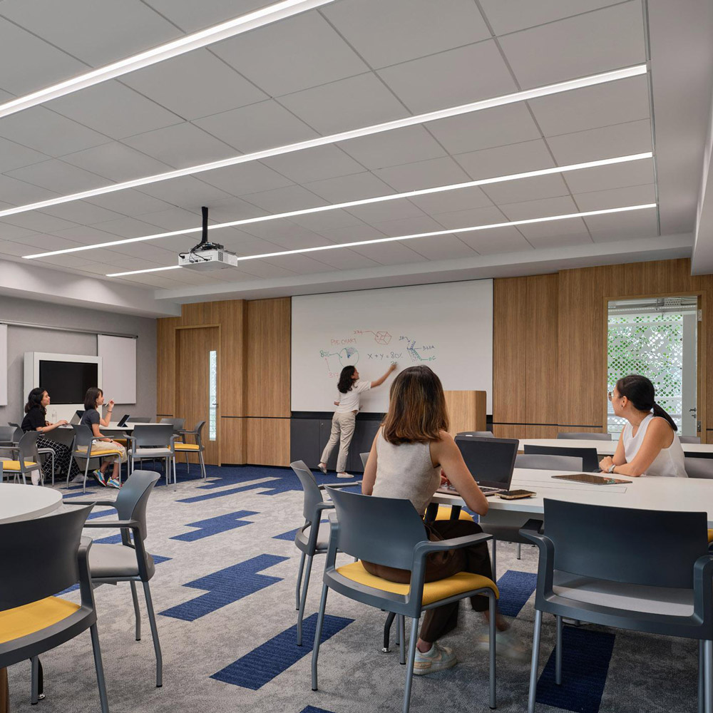 Aedas’s James Cook University Singapore interior is shown as a contemporary flexible teaching classroom with reconfigurable tables, integrated audiovisual systems, acoustic ceiling panels, and perimeter glazing. The image highlights technology‑enabled learning spaces, zoned circulation, and interior architecture designed to support both collaborative and focused study modes.