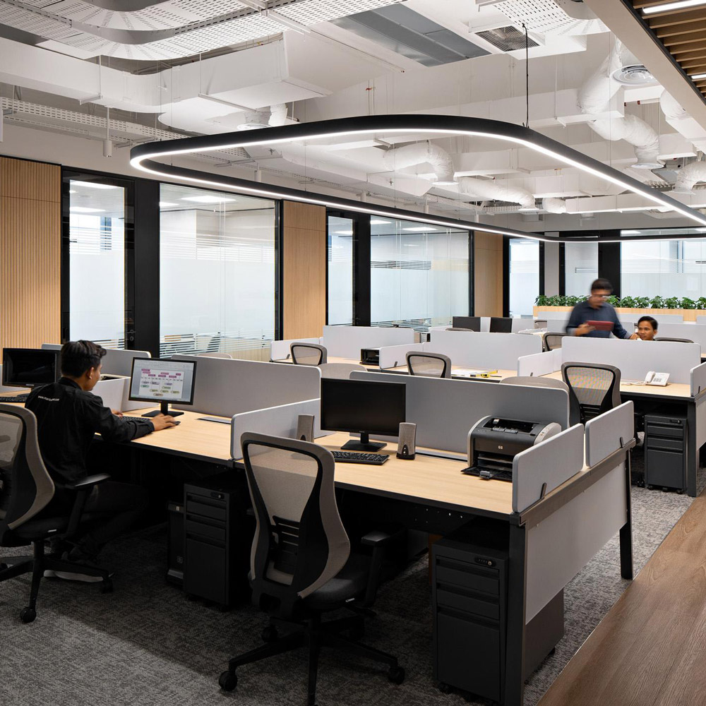 Aedas’s Napan Persada office in Jakarta is shown as a contemporary open‑plan workplace with customised workstations, integrated timber feature walls, exposed services ceiling, and linear suspended lighting. The image highlights client‑fabricated furniture, modular desk systems, and a balanced layout supporting collaboration and focused work within a CBD office environment.
