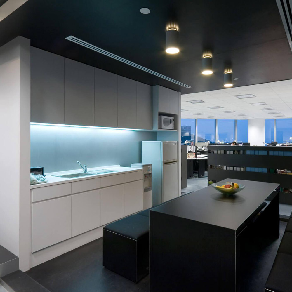Aedas Interiors’ M&C Saatchi Hong Kong office is shown as a bold monochromatic workplace with black and white finishes, exposed raised‑floor panels, and minimalist kitchen and breakout areas. The image highlights cost‑efficient interior architecture using restrained materials, integrated lighting, and open planning to create a strong brand identity without physical separation between reception and open office zones.