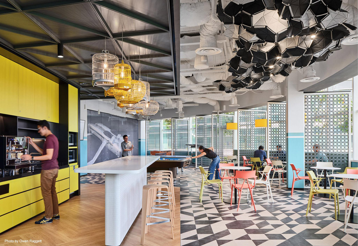 Aedas Interiors’ Autodesk Client Experience Centre in Singapore is shown as a multifunctional collaboration space with geometric ceiling installations, open social seating, a feature bar counter, and patterned flooring. The image highlights adaptive workplace interiors designed to support client engagement, informal collaboration, and creative showcase environments.