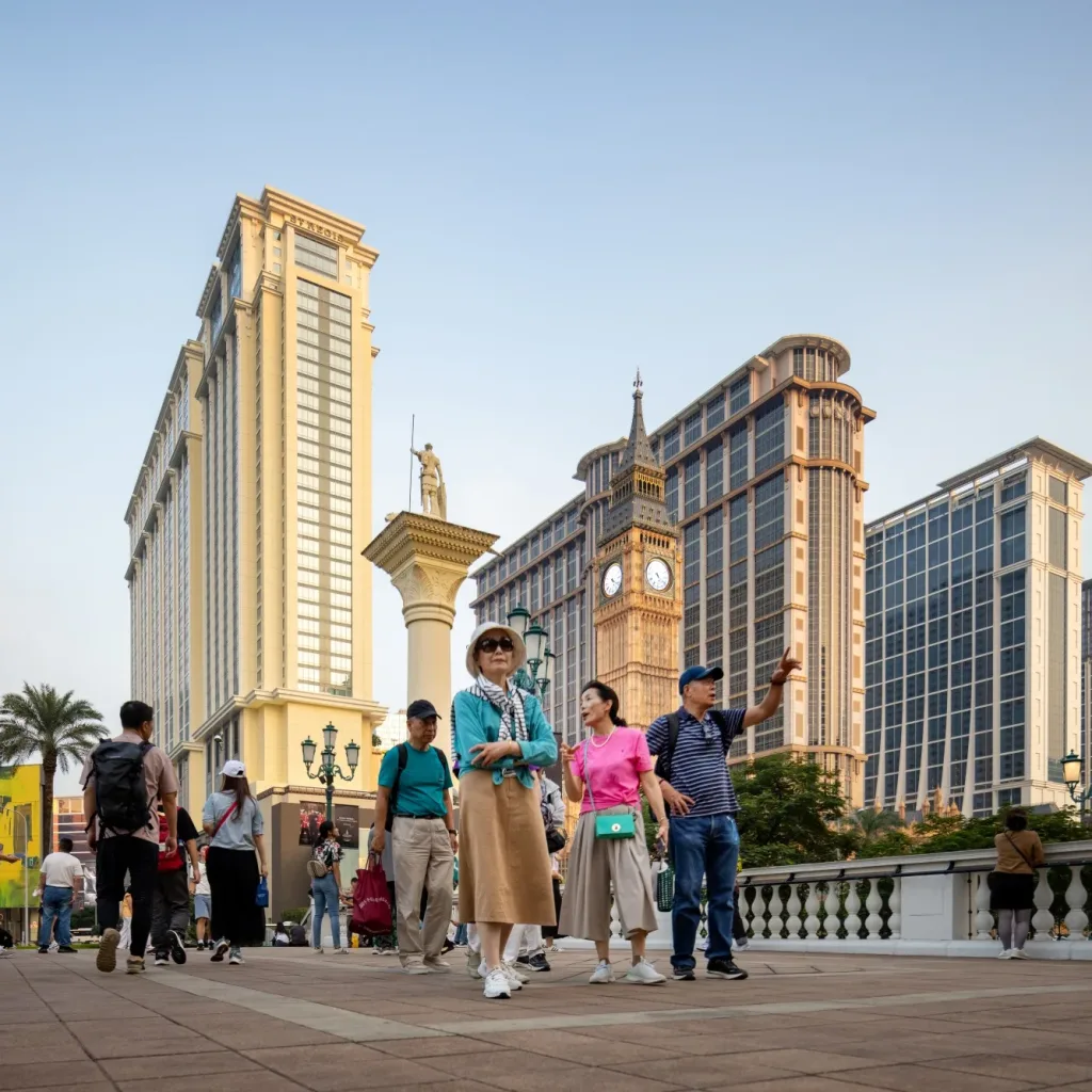 Aedas’ Londoner Macao integrated resort promenade with hotel towers, classical façades and public realm at Cotai. Street‑level view of Aedas‑designed The Londoner Macao, showing a pedestrian promenade framed by multi‑storey hotel towers with classical detailing, glazed façades and articulated cornices. Replica landmark elements and lantern‑style street lighting define the public realm, with podium levels accommodating retail entrances and covered walkways within the Cotai integrated‑resort district.