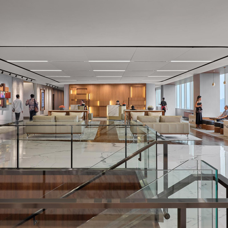 Aedas Interiors’ PwC Jakarta office is shown as a vertical campus environment with open social lounge seating, transparent balustrades, warm timber feature walls, and integrated circulation linking multiple floors. The image highlights non‑assigned workplace planning, layered work zones, and a human‑centric corporate interior supporting collaboration and mobility.