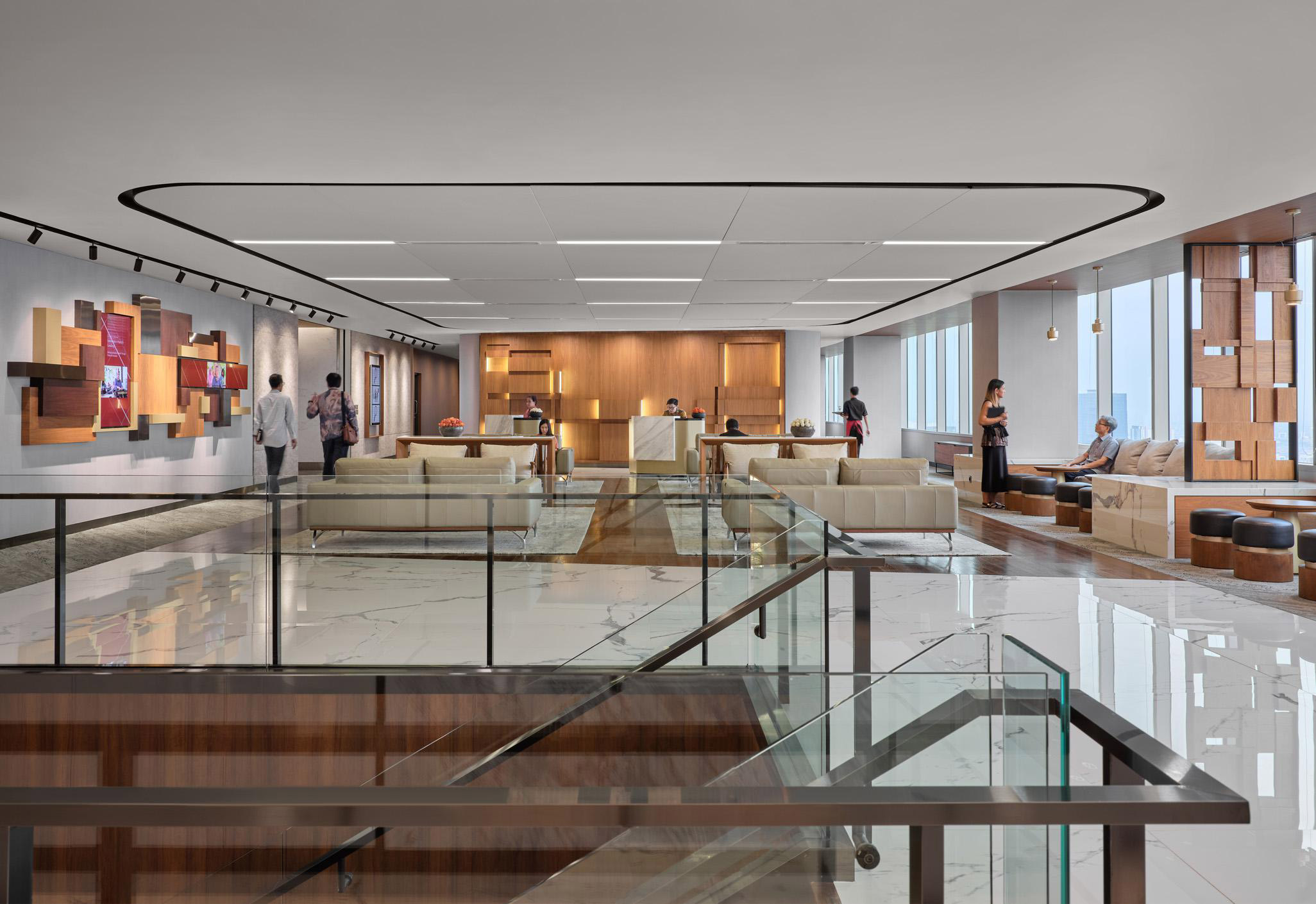 Aedas Interiors’ PwC Jakarta office is shown as a vertical campus environment with open social lounge seating, transparent balustrades, warm timber feature walls, and integrated circulation linking multiple floors. The image highlights non‑assigned workplace planning, layered work zones, and a human‑centric corporate interior supporting collaboration and mobility.