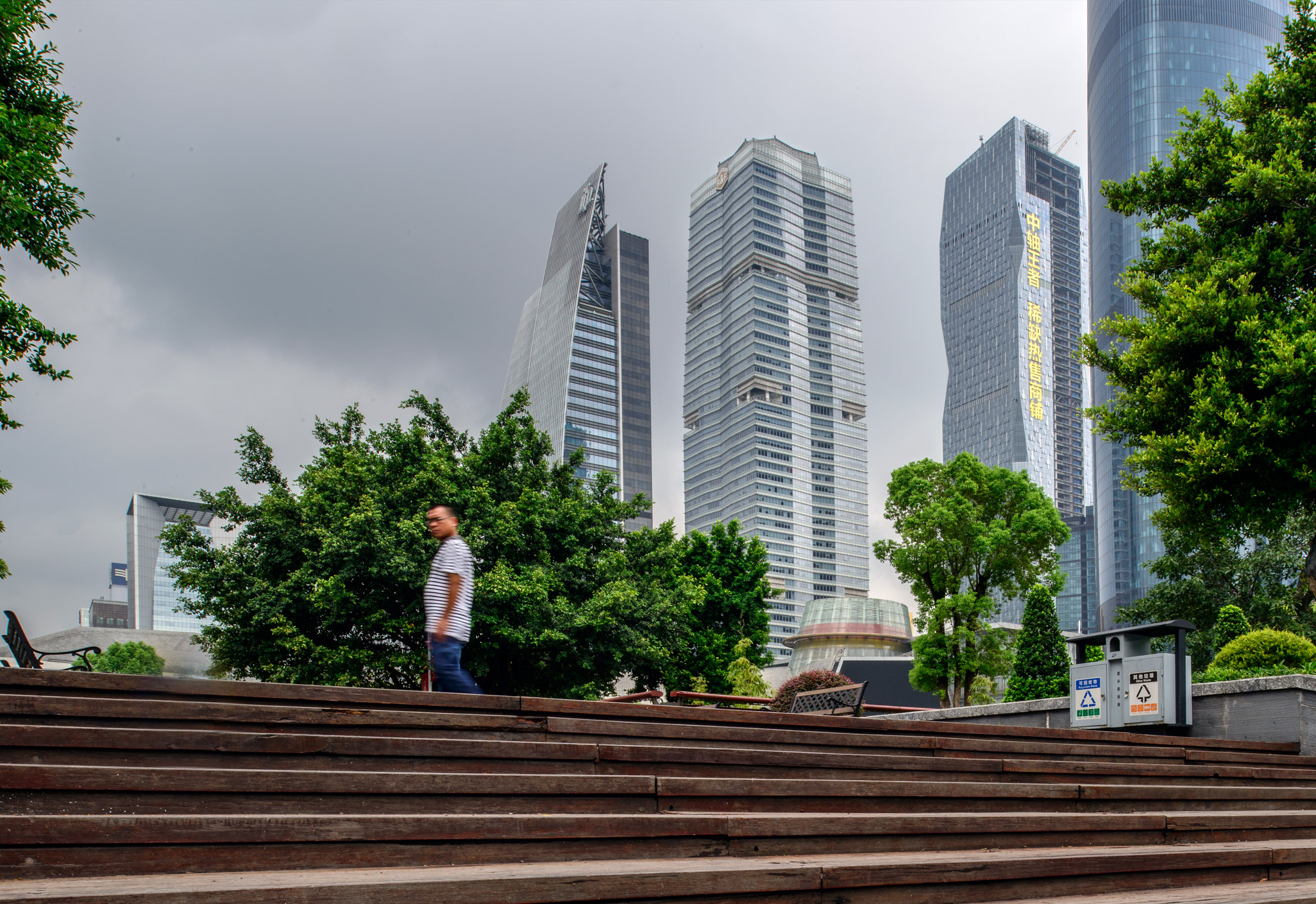Aedas’s R&F Center in Guangzhou is shown as a tall, rectilinear office tower with a translucent glass façade rising prominently within the city’s central business district. The ground‑level view highlights the tower’s elegant proportions, refined curtain wall system, and integration with landscaped public space and surrounding high‑rise buildings.
