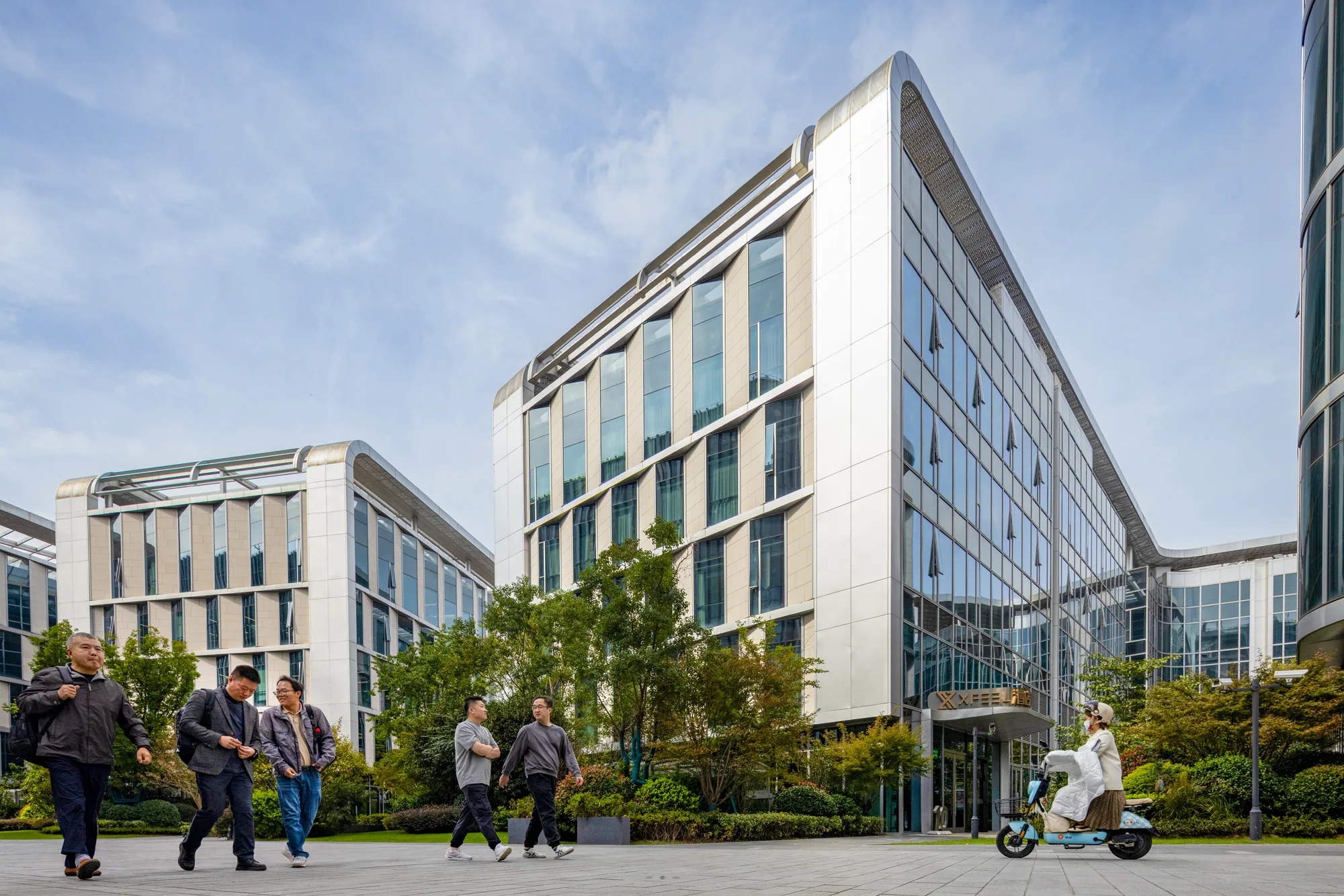 Aedas’s Shanghai BU Centre is shown as a mixed‑use campus with mid‑rise and low‑rise office buildings articulated by vertical glazing, solid cladding panels, and integrated landscape courtyards. The street‑level view highlights pedestrian‑oriented public open space, transparent ground floors, and a calm urban office environment in Qingpu.