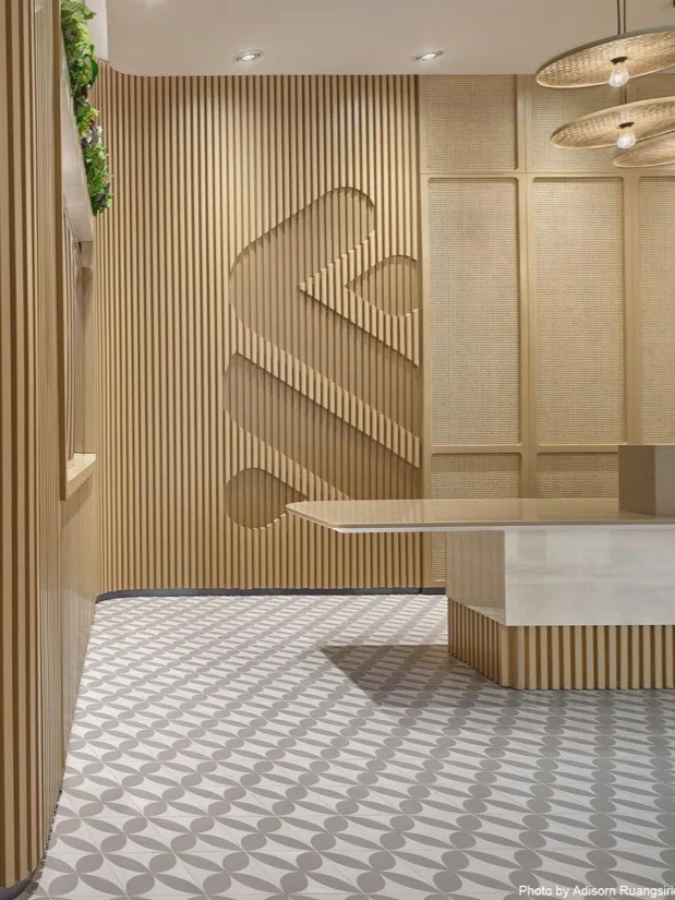 Aedas’s Standard Chartered Bank Bangkok office interior is shown with a human‑centric connect zone comprising timber slat partitions, integrated meeting booth, patterned flooring, and suspended feature lighting. The image highlights modular collaboration spaces, acoustic zoning, and contemporary financial‑workplace interiors designed for flexibility and social interaction.