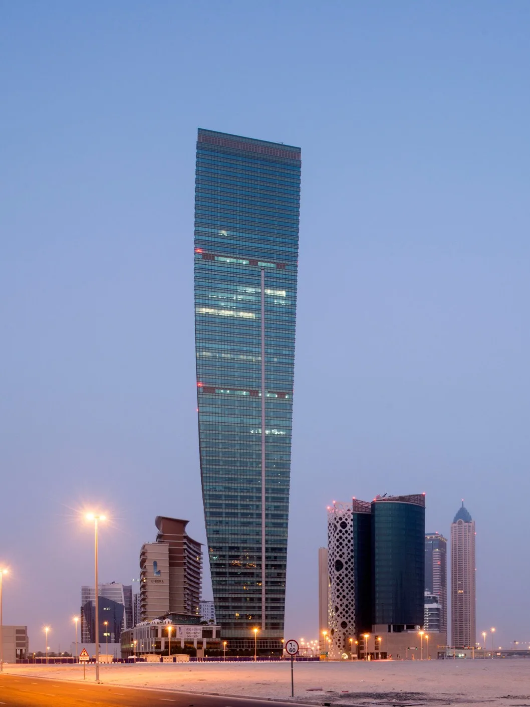 Aedas’s U‑Bora Towers in Dubai is shown as a landmark high‑rise complex dominated by a 263‑metre office tower with a gently curving, tapered form. The skyline view highlights the tower’s shallow twist, vertical glazing, and its relationship to a low‑rise podium and surrounding Business Bay towers.