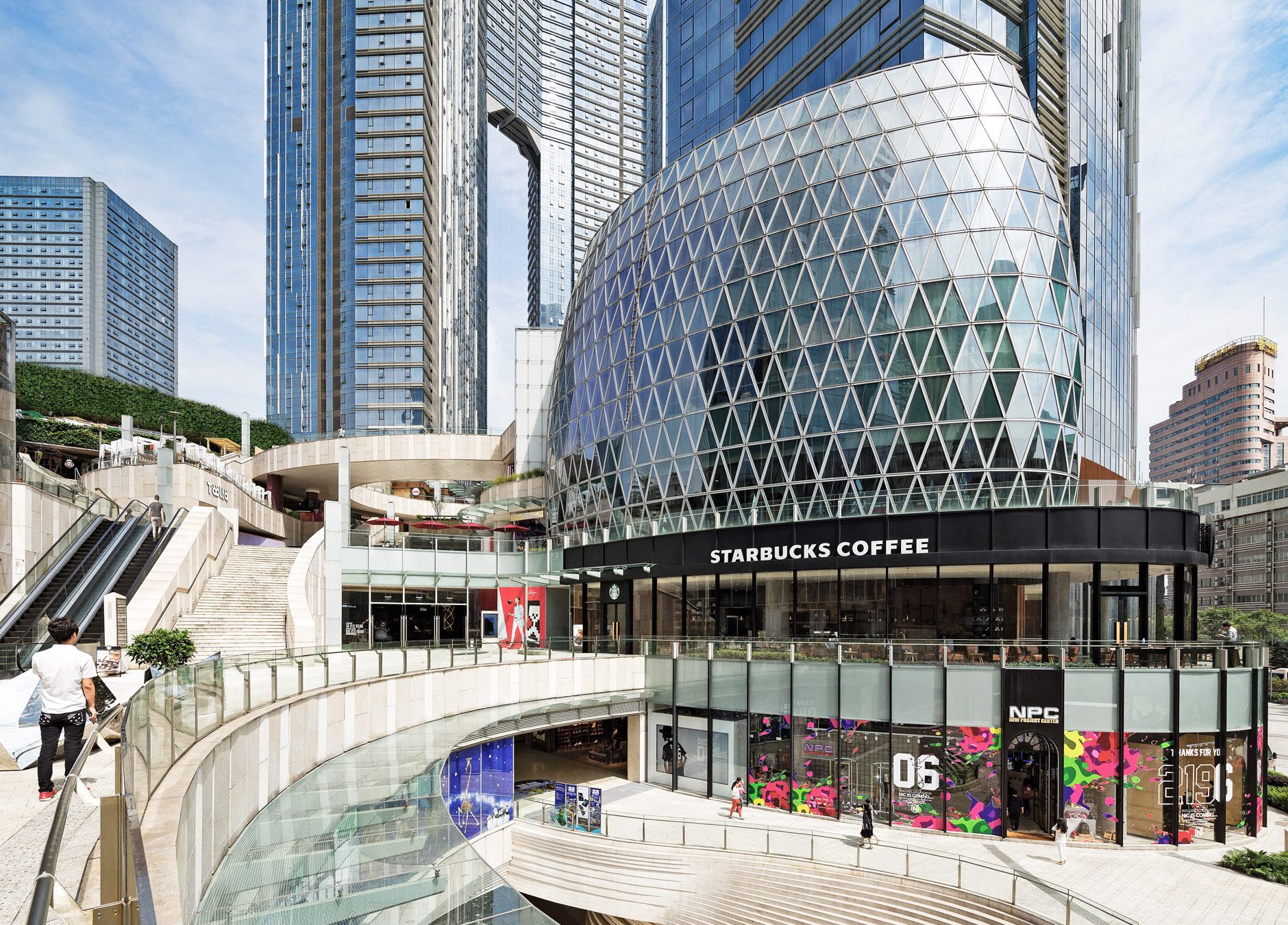 Aedas’s Huazhi Plaza in Chengdu is shown as a mixed‑use urban complex featuring a sculptural diamond‑patterned retail pavilion, stepped public terraces, and surrounding high‑rise towers. The street‑level view highlights multi‑level pedestrian circulation, transparent retail frontage, and integration with a dense city centre environment near Chunxi Road.