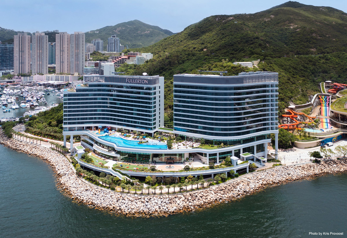 Aedas’ Fullerton Ocean Park Hotel with twin streamlined towers and cascading podium terraces along Hong Kong’s south coast. Aerial view of the Aedas‑designed Fullerton Ocean Park Hotel Hong Kong, showing two curved hotel towers with horizontal façade banding atop a stepped podium. The cascading terraces face the South China Sea, integrating outdoor pools and landscaped decks, while the complex is embedded between the rocky shoreline and the green hillside of Brick Hill.