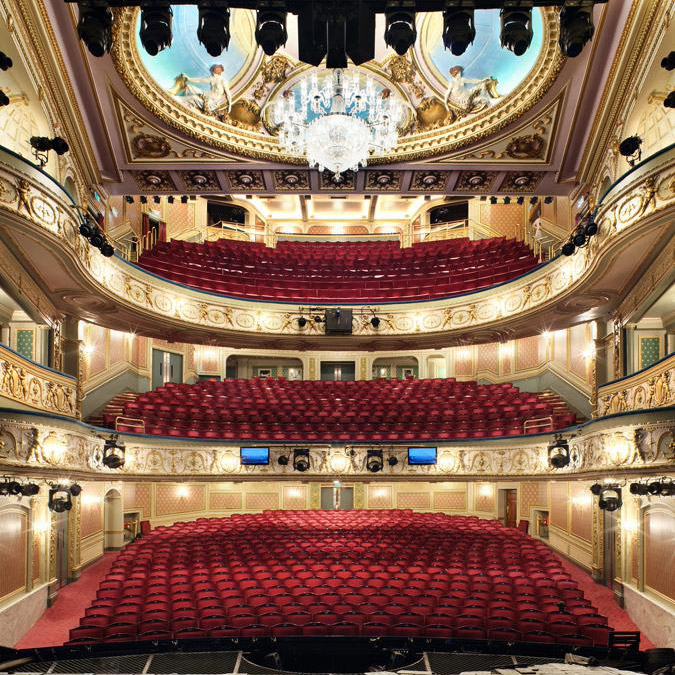 Aedas’s Sondheim Theatre in London is shown with a richly articulated historic theatre volume featuring a central domed ceiling, layered proscenium arch, and ornamental structural detailing. The image highlights heritage performance architecture, integrated building systems, and preservation‑led theatre design within a dense West End urban context.