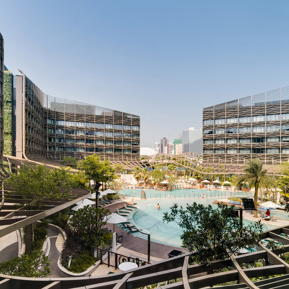 Aedas’s Ocean Park Marriott Hotel in Hong Kong is shown as a resort hotel composed of three L‑shaped accommodation blocks enclosing a central landscaped courtyard with swimming pool. The image highlights layered balcony façades, curved circulation terraces, and a podium‑integrated leisure core positioned at the entrance to Ocean Park.