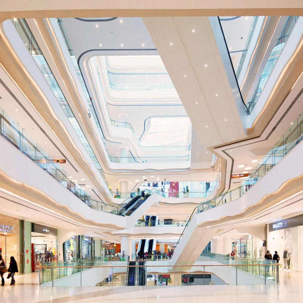 Aedas Interiors’ Starlight Place in Chongqing is shown as a multi‑storey retail atrium with fluid, sculptural white balcony forms, integrated escalators, and continuous ribbon‑like ceiling lighting. The image highlights a dynamic shopping‑mall interior where contrasting curves and straight lines, light and shadow, and smooth surfaces create a visually layered circulation space that draws visitors upward through the mall.