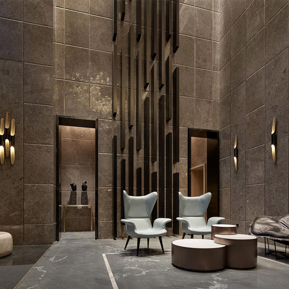 Aedas Interiors’ One Avenue Tianyuan show flat in Shenzhen is shown as a dramatic double‑height interior with stone‑clad walls, sculptural vertical metal installation, refined lounge seating, and soft accent lighting. The image highlights an understated luxury residential environment where European contemporary elegance is blended with Chinese influences through rich materials, geometric spatial order, and bespoke detailing.