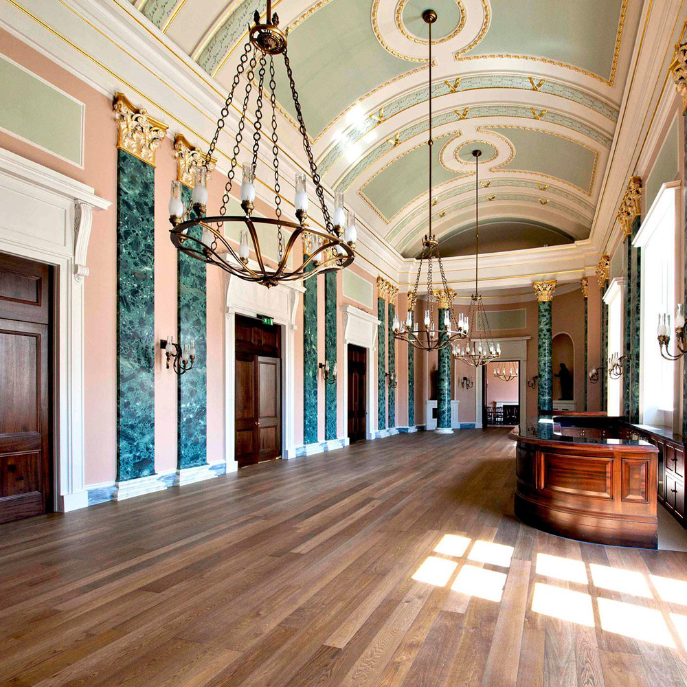 Aedas’s Theatre Royal Drury Lane is shown with a grand internal gallery architecture featuring a vaulted ceiling, axial spatial layout, marble‑clad columns, timber flooring, and integrated chandeliers. The image highlights heritage theatre architecture, ceremonial circulation space, and performance‑supporting civic structure within London’s West End.