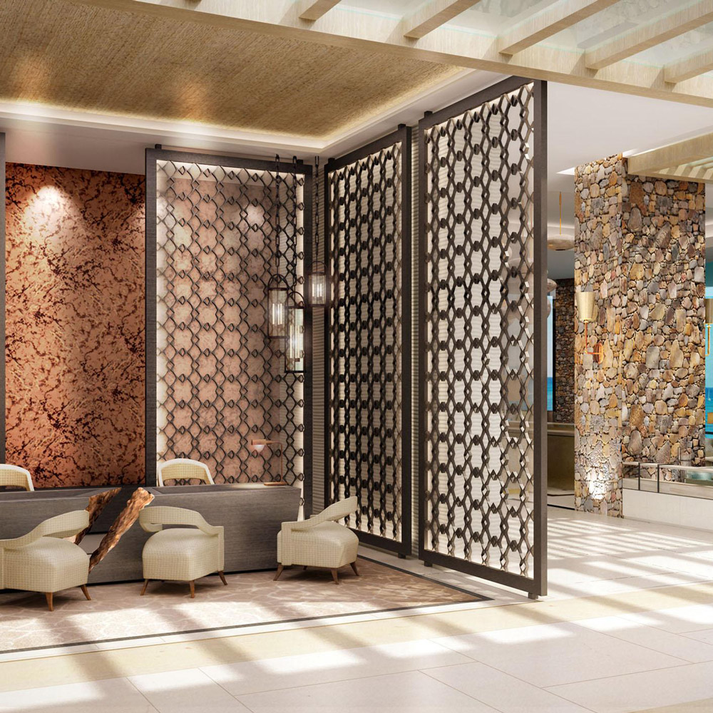 Aedas Interiors’ proposed Jumeirah Saraya Bandar Jissah Resort 1 in Muscat is shown as a luxurious lounge setting with layered stone walls, intricate Islamic‑patterned screens, light timber ceilings, and soft upholstered seating. The image highlights a refined resort interior where natural textures, filtered daylight, and crafted detailing evoke coastal, garden, and mountain inspirations within an elegant hospitality environment.
