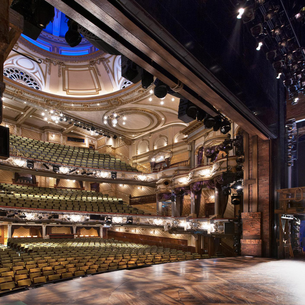Aedas’s Victoria Palace Theatre in London is shown as a historic proscenium theatre architecture with a deep stage house, multi‑tiered balconies, ornamental structural detailing, and integrated lighting infrastructure. The image highlights heritage theatre massing, sectional organization, and performance‑led architectural volume within a dense West End context.
