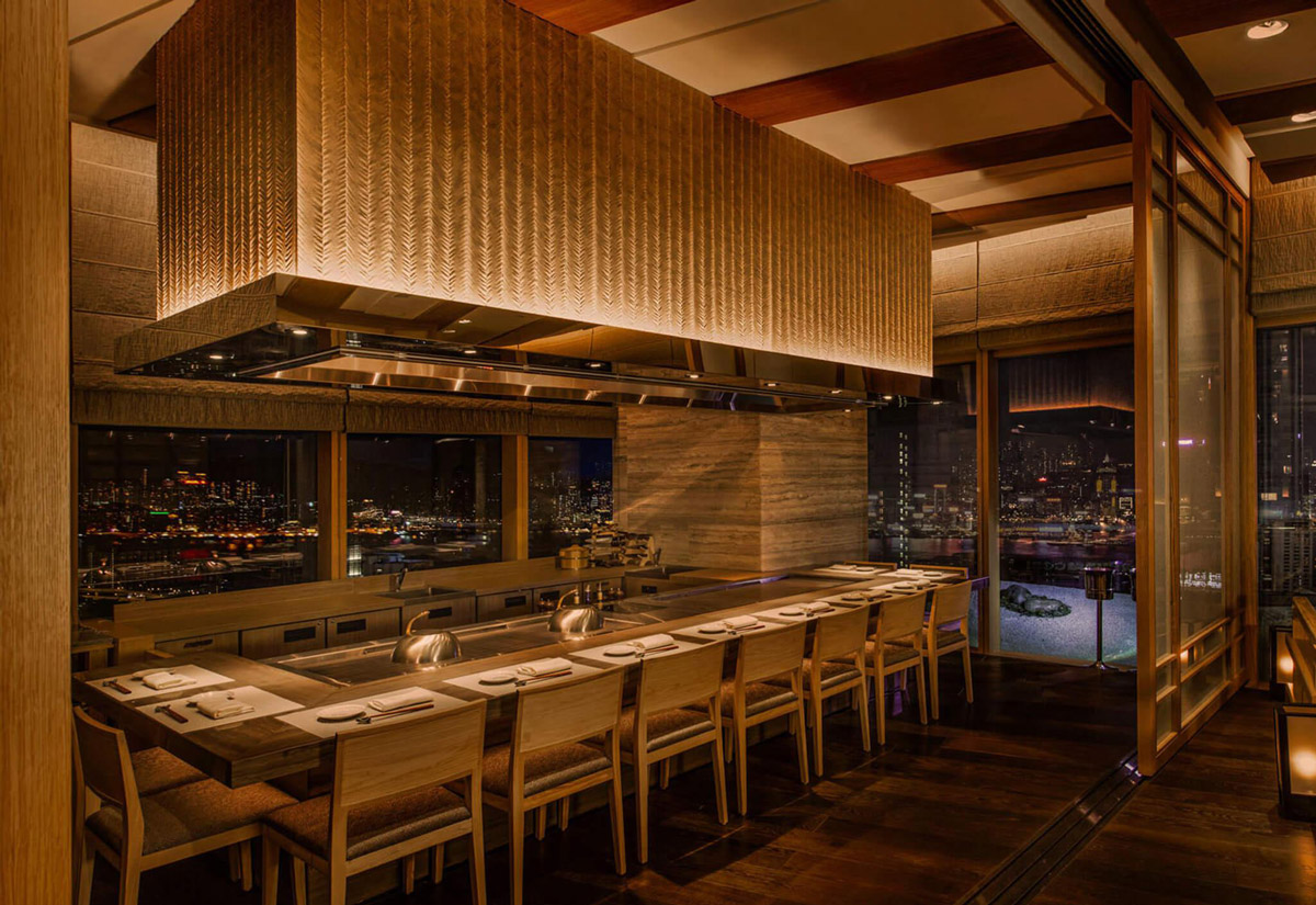 Aedas Interiors’ Kyo‑Shun in Hong Kong is shown as a refined Japanese dining interior featuring a long timber sushi counter, woven-texture feature ceiling, warm wood flooring, and minimalist seating. The image highlights a tranquil hospitality environment characterised by natural materials, subdued lighting, and craftsmanship‑driven detailing that frames the culinary experience with calm elegance.