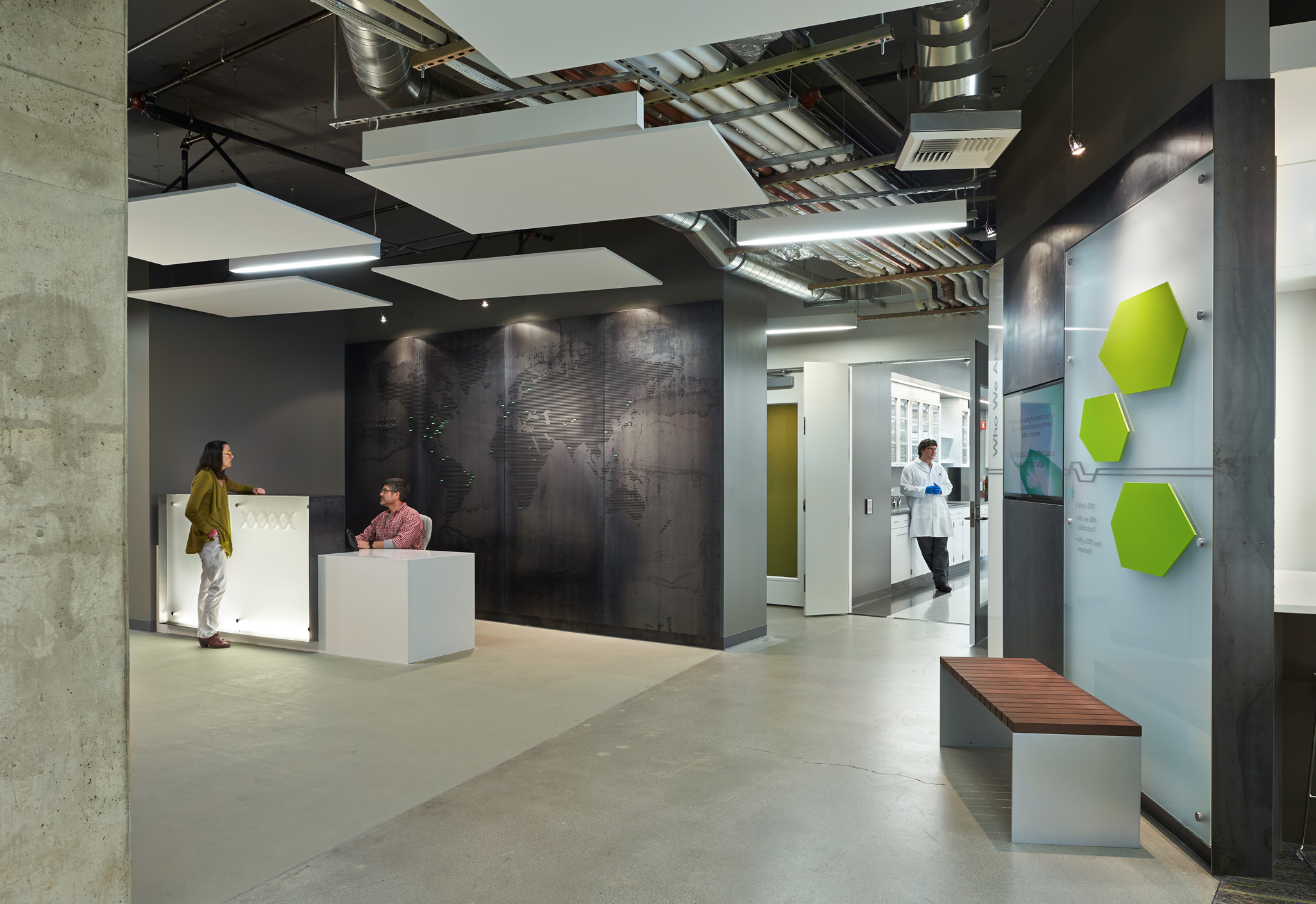 Aedas’s Infectious Disease Research Institute in Seattle is shown with an open research workplace featuring exposed concrete structure, visible mechanical services, suspended acoustic ceiling panels, integrated lighting, and flexible modular partitions. The interior highlights laboratory‑adjacent office architecture designed for collaboration within a controlled research environment.