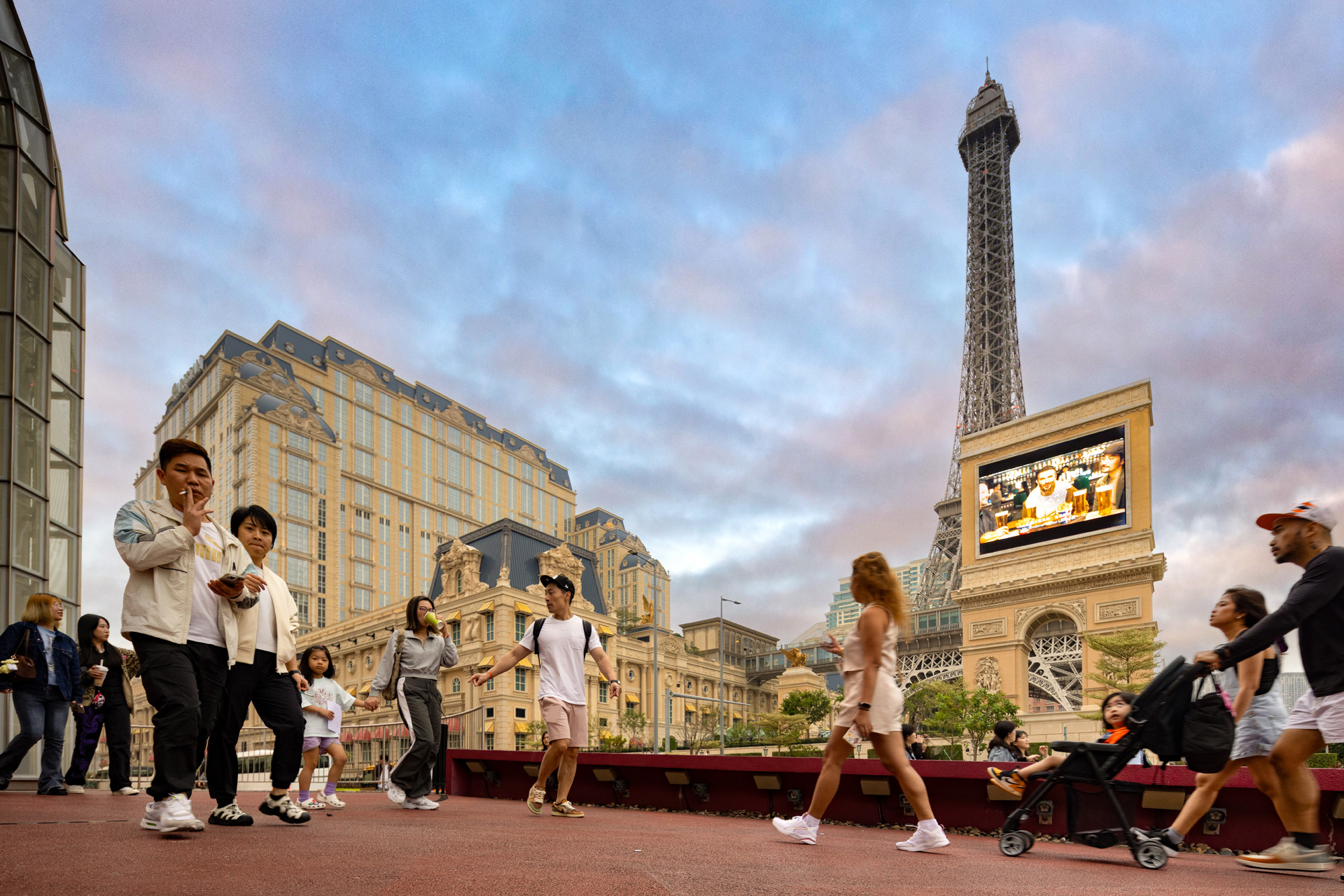 Aedas’ Parisian Macao integrated resort with Eiffel‑Tower replica, hotel façades and pedestrian public realm on Cotai. Street‑level view of Aedas‑designed The Parisian Macao, showing a pedestrian promenade framed by hotel towers with classical European façades. A full‑scale Eiffel Tower replica anchors the resort skyline, while podium levels integrate retail entrances, gaming access and covered walkways, supporting high visitor circulation within Macau’s dense Cotai Strip.