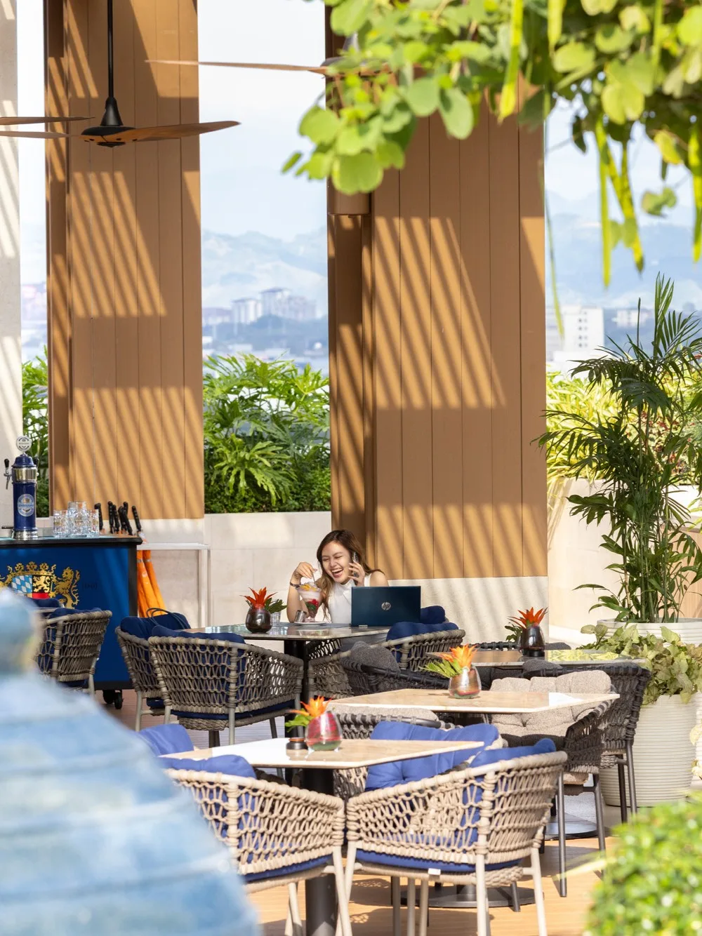 Aedas’s Solaire North in Quezon City is shown with a shaded semi‑outdoor terrace defined by vertical timber screens, open structural bays, integrated planting, and flexible dining seating. The image highlights climate‑responsive hospitality architecture, passive shading strategies, and seamless indoor‑outdoor spatial integration within a large integrated resort.