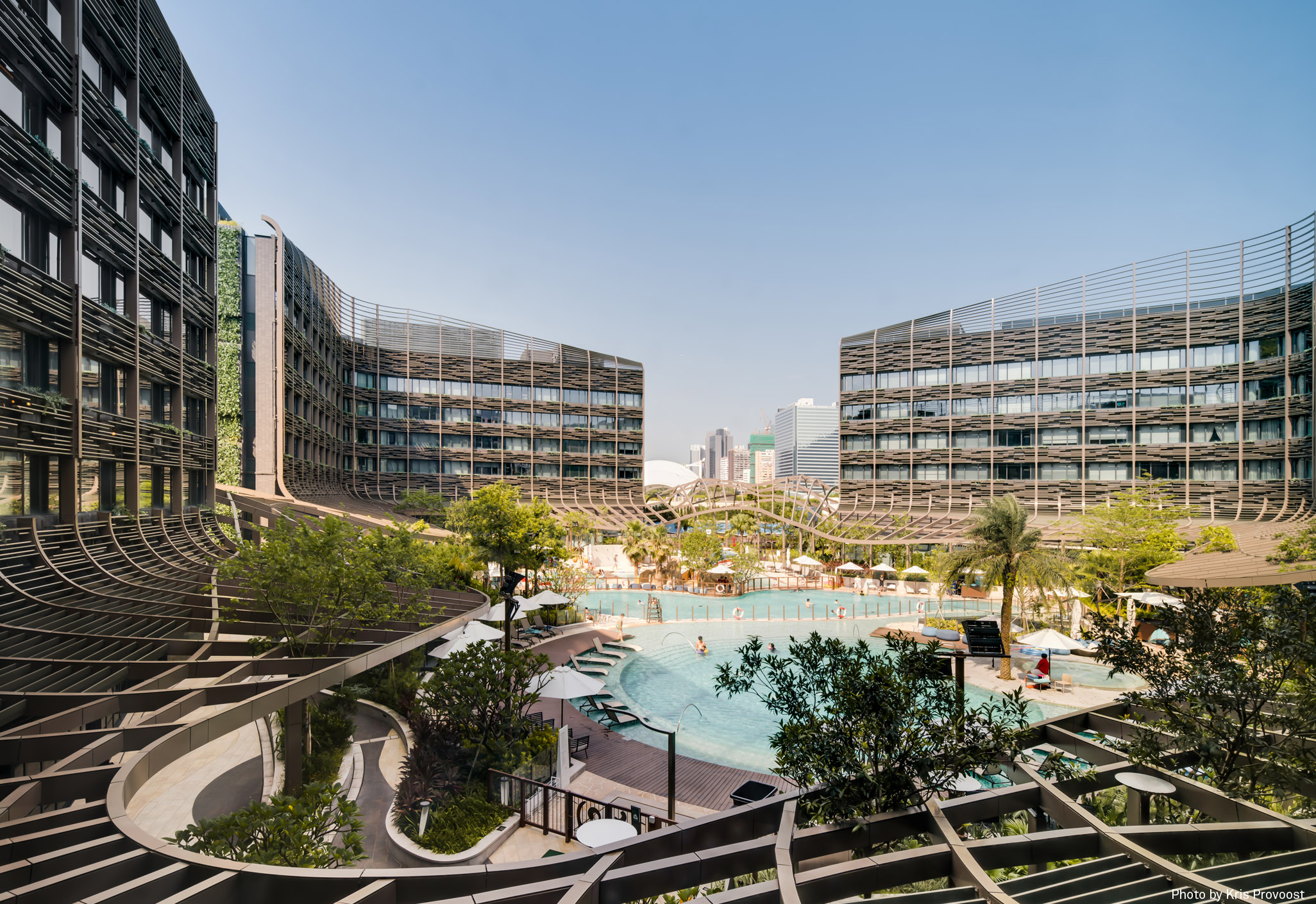 Aedas’s Ocean Park Marriott Hotel in Hong Kong is shown as a resort hotel composed of three L‑shaped accommodation blocks enclosing a central landscaped courtyard with swimming pool. The image highlights layered balcony façades, curved circulation terraces, and a podium‑integrated leisure core positioned at the entrance to Ocean Park.