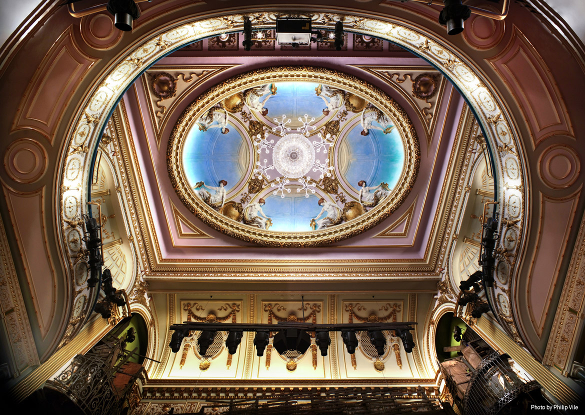 Aedas’s Sondheim Theatre in London is shown with a richly articulated historic theatre volume featuring a central domed ceiling, layered proscenium arch, and ornamental structural detailing. The image highlights heritage performance architecture, integrated building systems, and preservation‑led theatre design within a dense West End urban context.