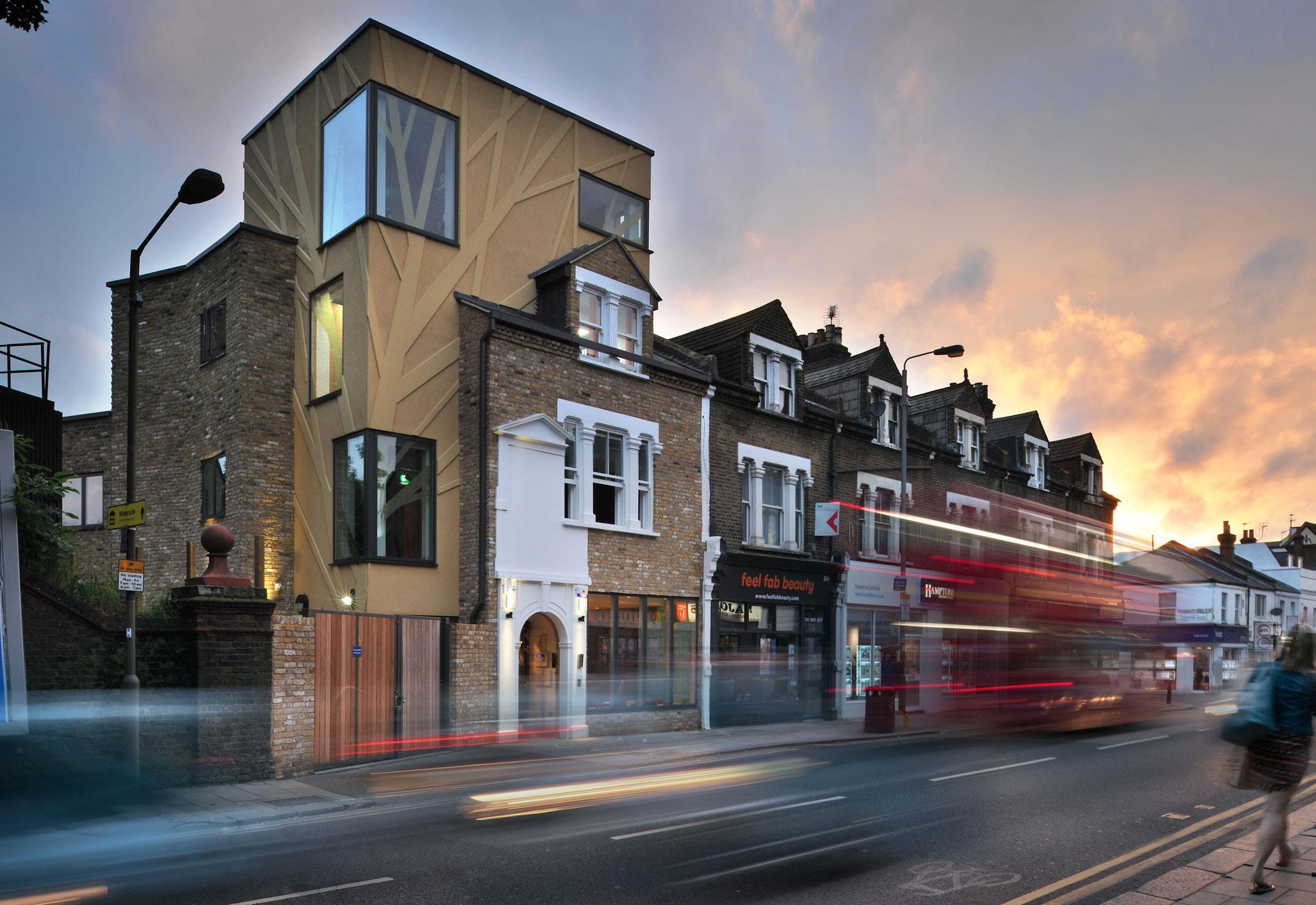 Aedas’s Tara Theatre in London is shown as a contemporary infill cultural building with angular massing, prefabricated façade panels, irregular window apertures, and a compact vertical form. The street‑level view highlights adaptive reuse, tight urban integration, and performance‑led architecture within a dense UK high‑street context.