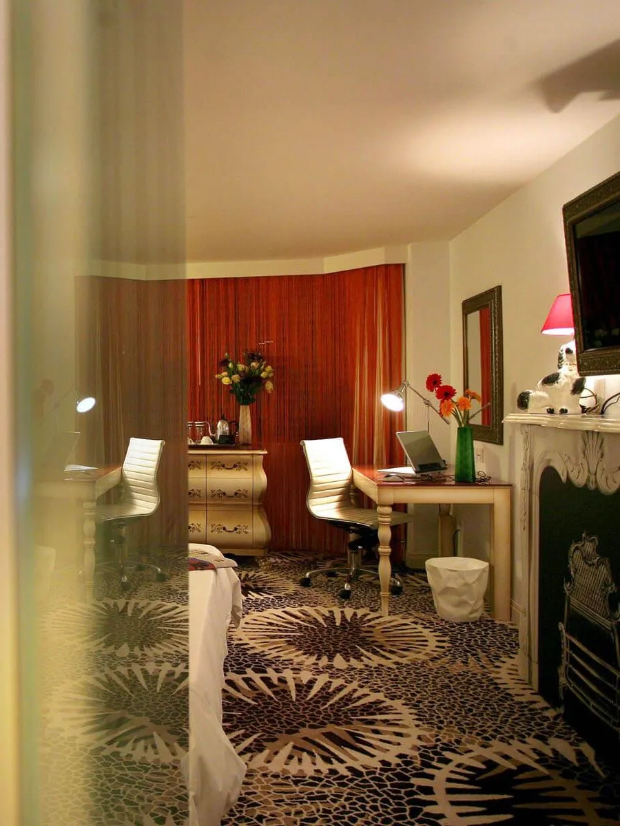 Aedas Interiors’ The Luxe Manor guest room in Hong Kong is shown as an eclectic boutique hotel interior combining vintage‑inspired furnishings, patterned carpeting, and layered lighting with contemporary detailing. The image highlights a playful yet refined accommodation space where traditional motifs, curated decorative elements, and bespoke furniture create a homely, theatrical atmosphere that reinterprets classic bedroom grandeur with a modern twist.