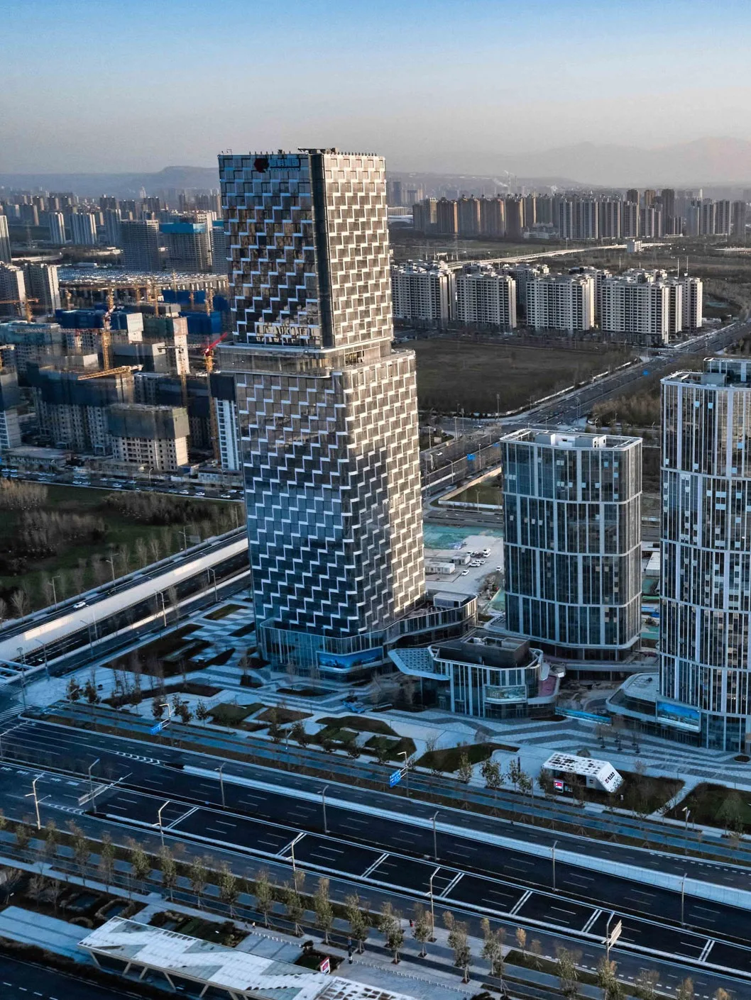 Aedas’s Xi’an Crystal Huixi Plaza is shown as a mixed‑use development of four towers with a highly articulated main tower clad in tessellated façade panels and three secondary towers rising from interconnected podiums. The aerial view highlights vertical density, podium‑based retail streets, and integrated public circulation within the International Port Area.