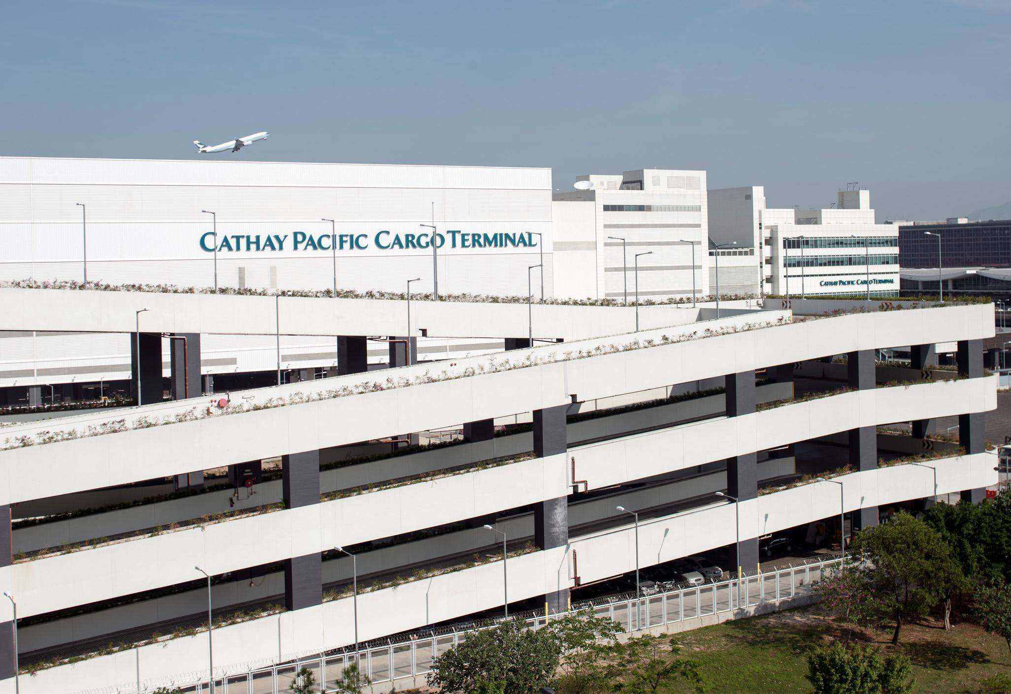 Aedas’ Cathay Pacific Cargo Terminal at Hong Kong International Airport is shown as a large‑scale logistics complex with linear white‑clad façades, horizontal louvers, and integrated service decks. The image highlights a highly efficient aviation infrastructure designed for high‑volume cargo handling, featuring clear functional articulation, expansive floor plates, and a streamlined architectural expression that reinforces Hong Kong’s role as a global air‑freight hub.