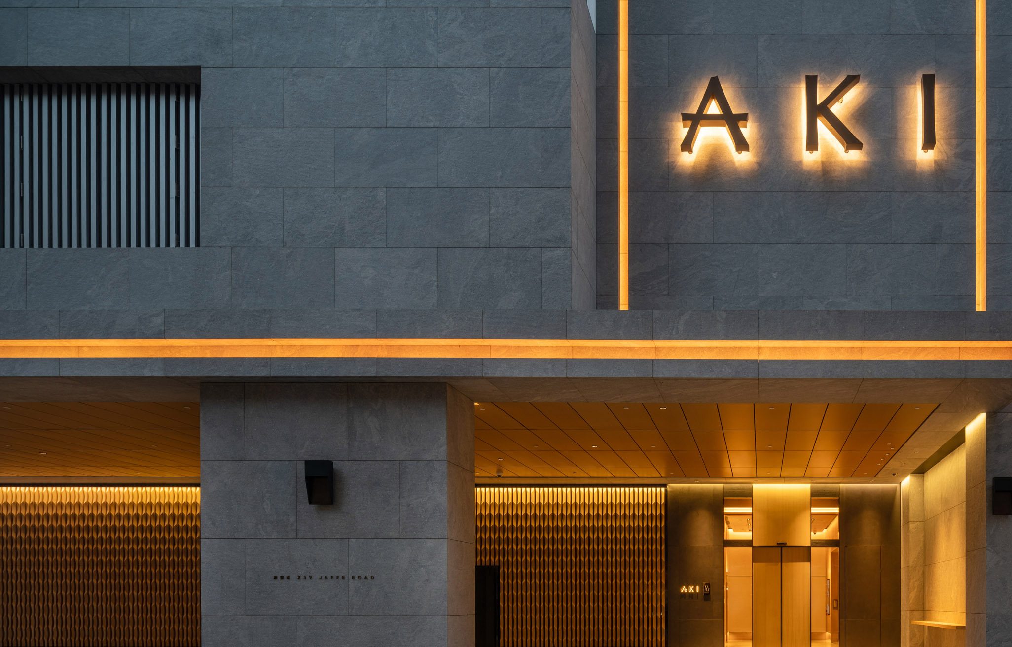 Aedas’s AKI Hong Kong – MGallery is shown with a refined urban hotel façade featuring dark stone cladding, sharp rectilinear geometry, recessed entrance canopy, and integrated illuminated signage. The exterior highlights boutique hospitality architecture, material restraint, and a controlled street‑level presence within a dense metropolitan context.