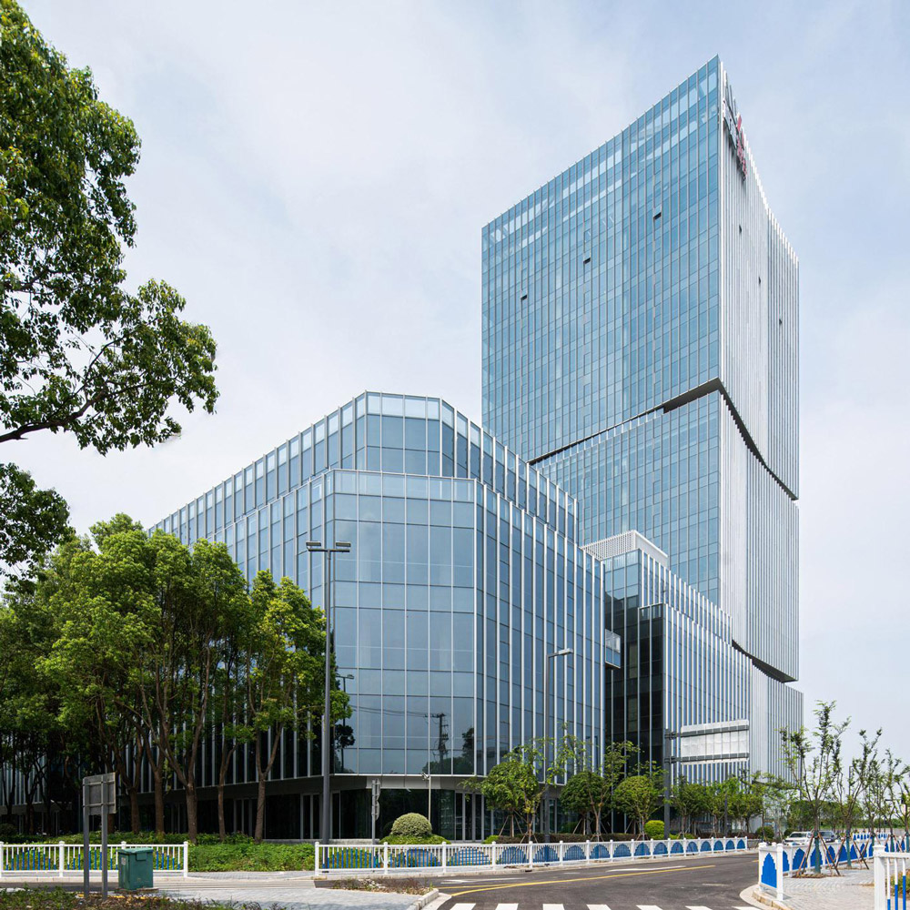 Aedas’ Shanghai Jiading Financial Center is shown as a contemporary office campus with a slender Grade‑A tower and lower‑rise office blocks set within dense greenery. The image highlights a crisp glass façade with articulated vertical fins, inward‑tapered sides, and outward‑extended corners, forming a light, elegant skyline that integrates seamlessly with the surrounding ecological landscape of Jiading New City.