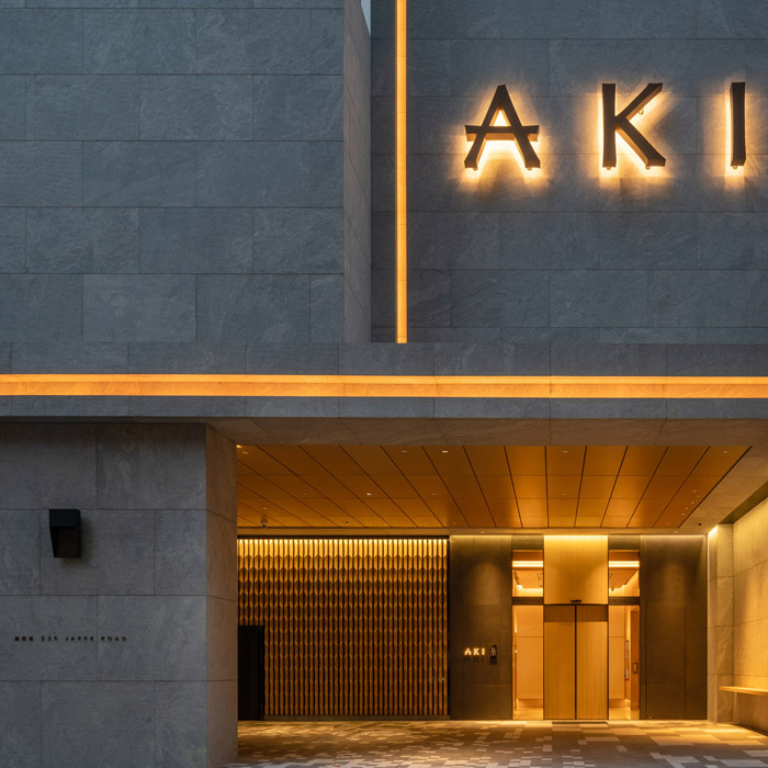Aedas’s AKI Hong Kong – MGallery is shown with a refined urban hotel façade featuring dark stone cladding, sharp rectilinear geometry, recessed entrance canopy, and integrated illuminated signage. The exterior highlights boutique hospitality architecture, material restraint, and a controlled street‑level presence within a dense metropolitan context.