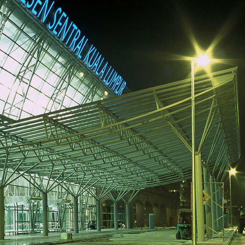 Aedas’ Kuala Lumpur Sentral is shown at night as a major transit concourse defined by expansive steel canopies and glass façades illuminated from within. The image highlights the hyperbolic paraboloid roof structure constructed in exposed steel and stainless steel cladding, framing the station entrance and conveying a sense of openness, movement, and civic scale befitting Malaysia’s primary integrated transport hub.